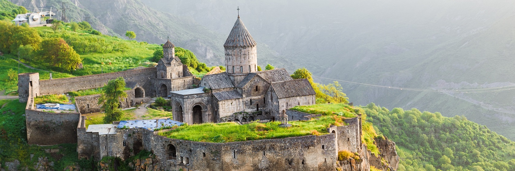 Tatevklostret i Armenien, som ligger p ett klipputsprng med branta bergssidor, dalen nedanfr r fylld av ljusgrna lvtrd.