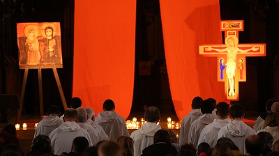 Interiör från Taizé med en samling människor, två upplysta röda tygstycken och ett krucifix.