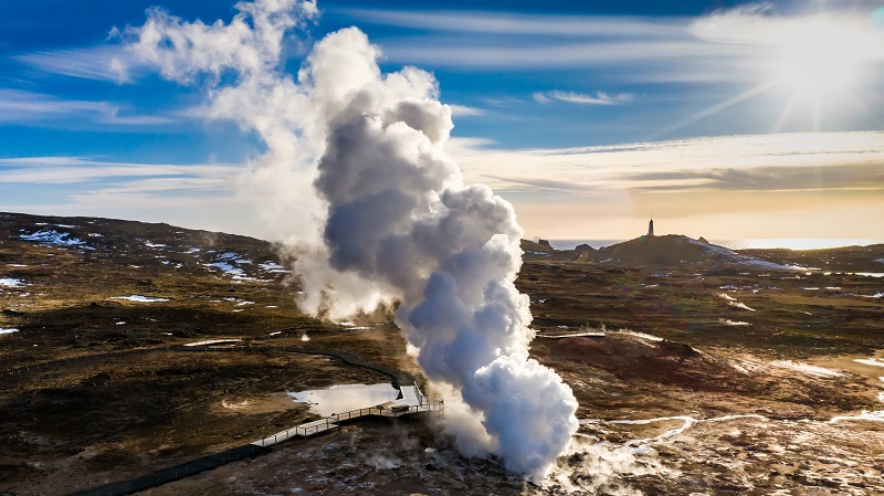 Ånga från en varm källa på Reykjanes stiger mot skyn, i ett svagt sluttande gräslandskap.