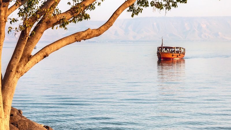 En turistb�t glider fram p� en stilla Gennesarets sj�, med Golanh�jderna p� andra sidan.