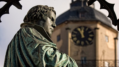 Kopparstaty av Martin Luther frn sidan i halvprofil, med ett suddigt kyrktorn i bakgrunden.