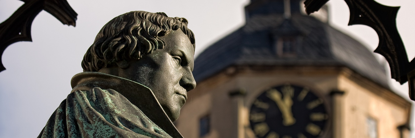 Kopparstaty av Martin Luther från sidan i halvprofil, med ett suddigt kyrktorn i bakgrunden.