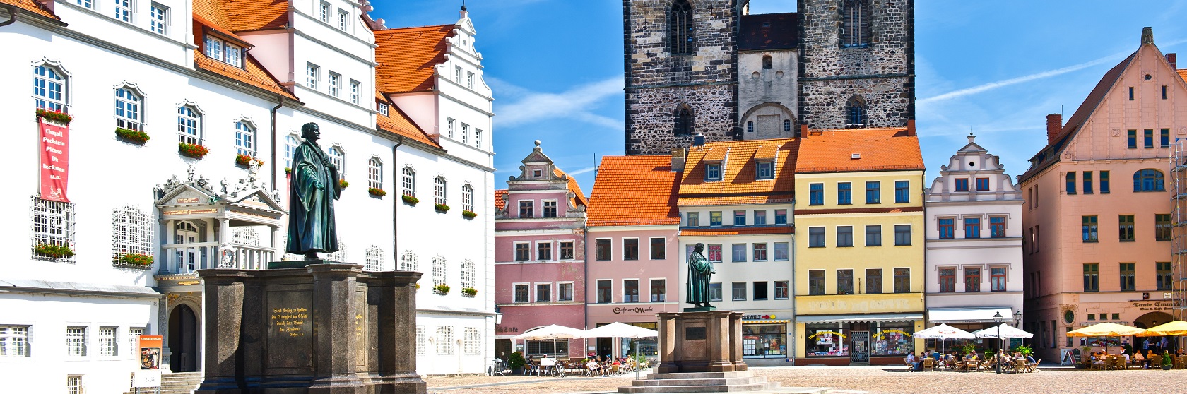 Staty av Luther mot medeltida bebyggelse och en klarbl� himmel, i Wittenberg.